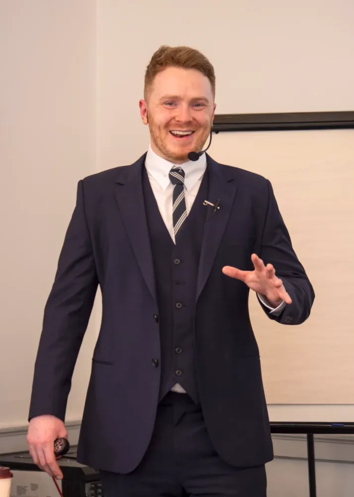 Dr. James Martin, founder of Dentists Who Invest, in a navy suit with a headset, presenting in front of a blank flip chart.